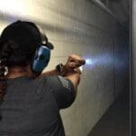 A woman is holding a gun and aiming it.