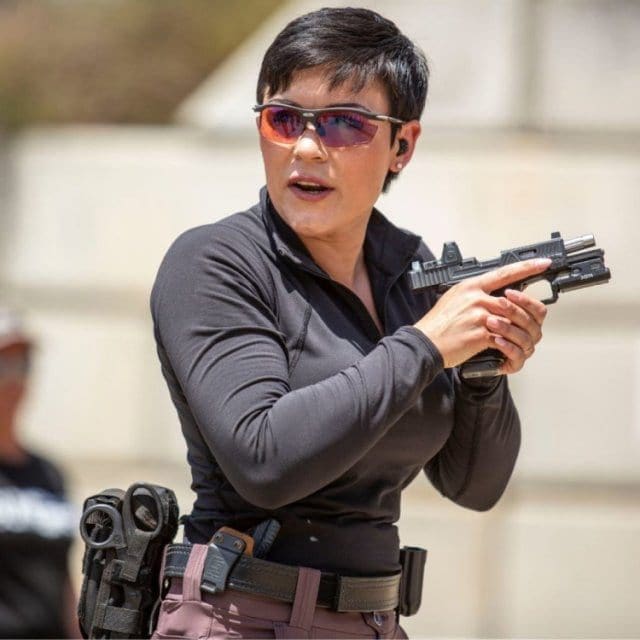 A woman holding a gun while wearing sunglasses.