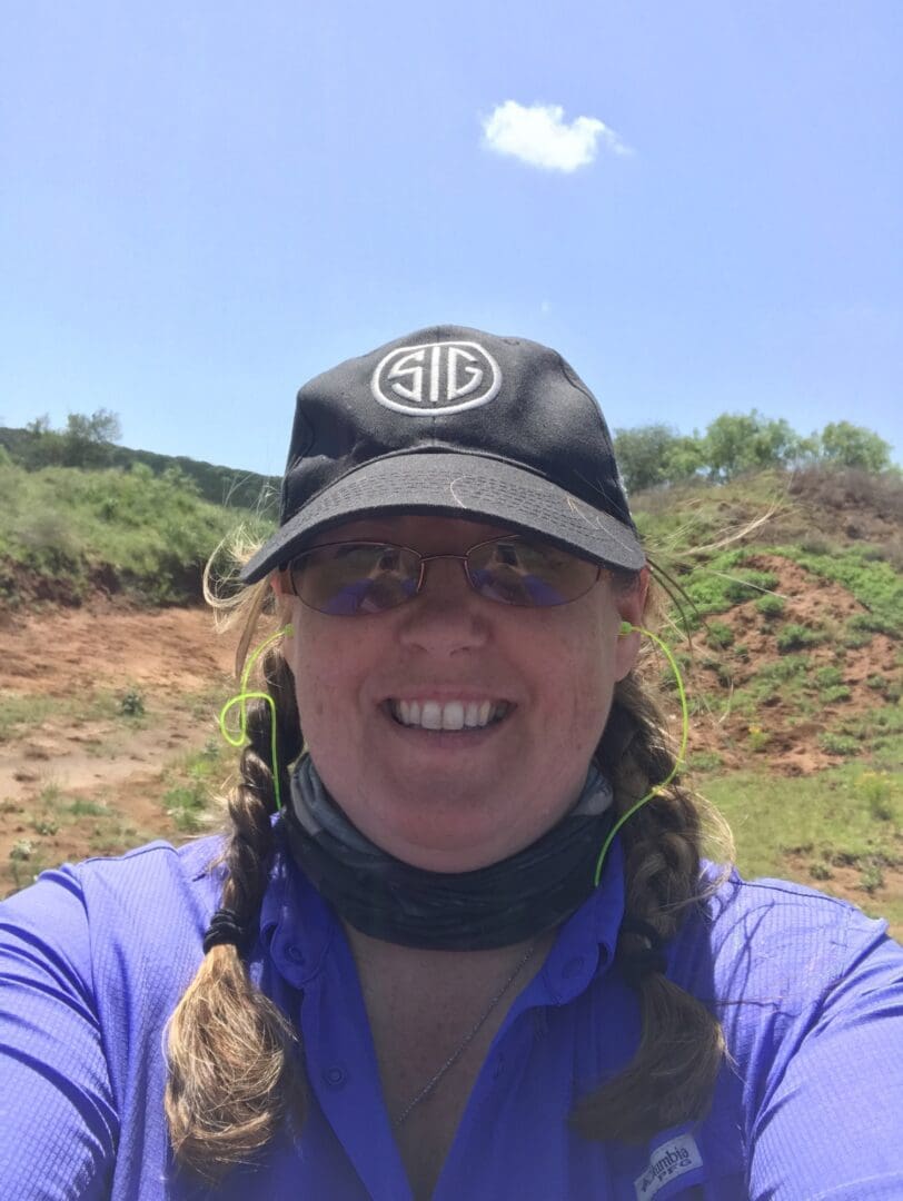 A woman in a hat and sunglasses standing on top of a hill.