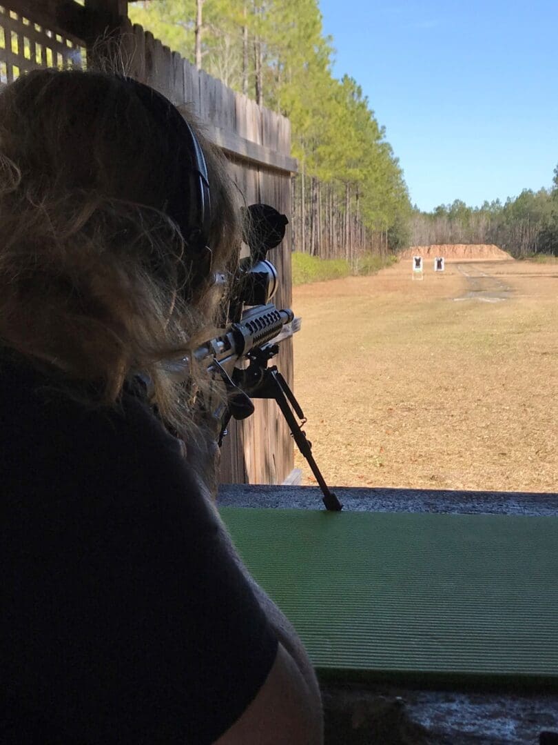 A woman is holding a gun and looking out the window.