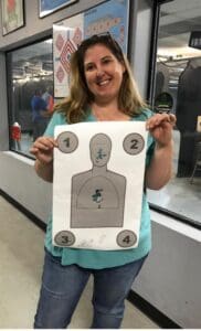 A woman holding up a paper target with the numbers 1-4 on it.