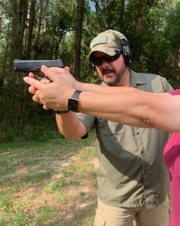 A man and woman holding guns in the woods.