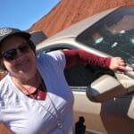 Smiling woman standing beside bullet-riddled car.