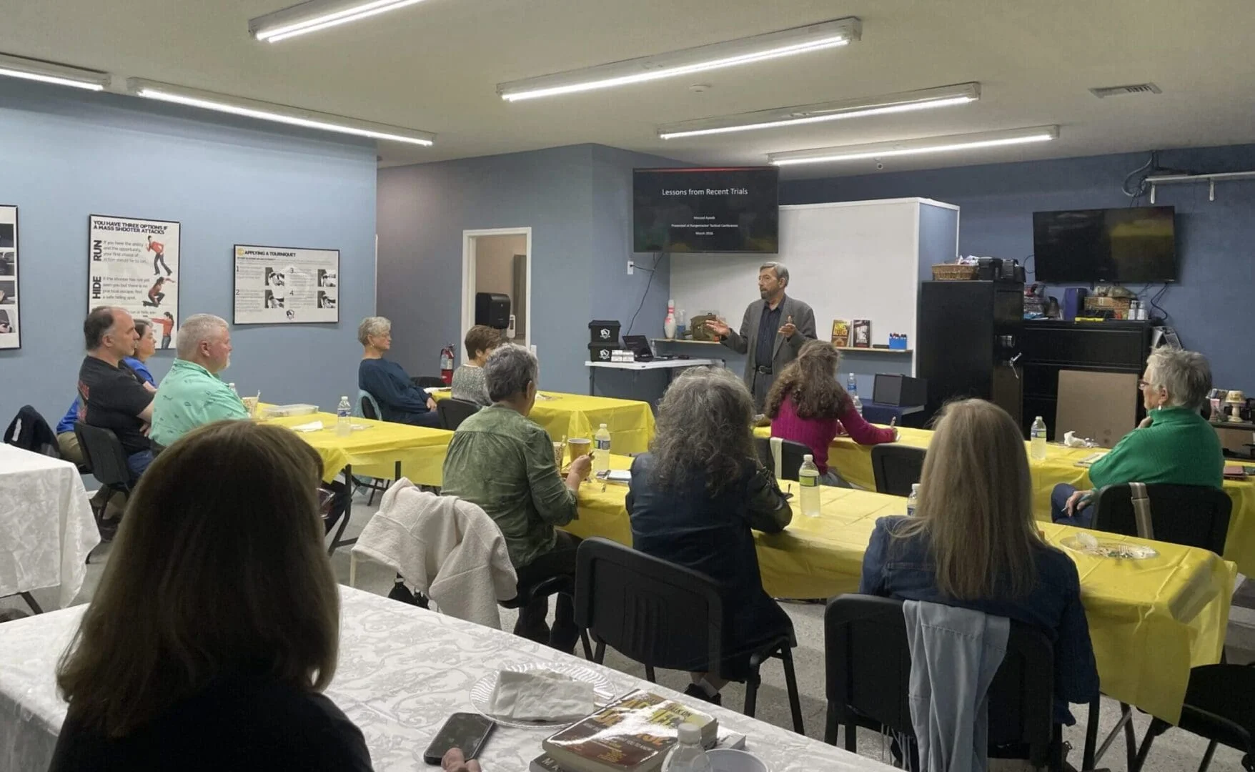 A group of people sitting around tables in front of yellow table cloths.